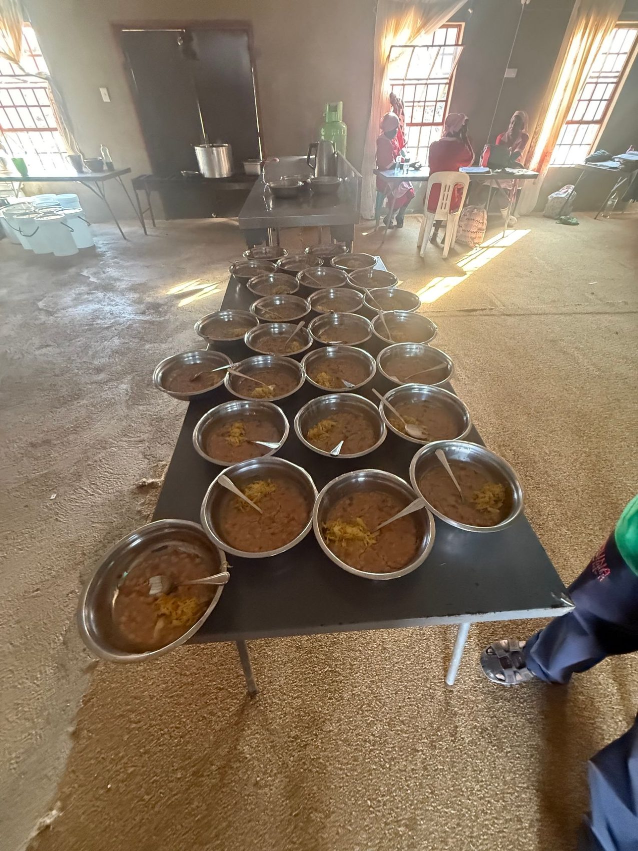 Rows of steel bowls filled with beans and cabbage, each with a spoon